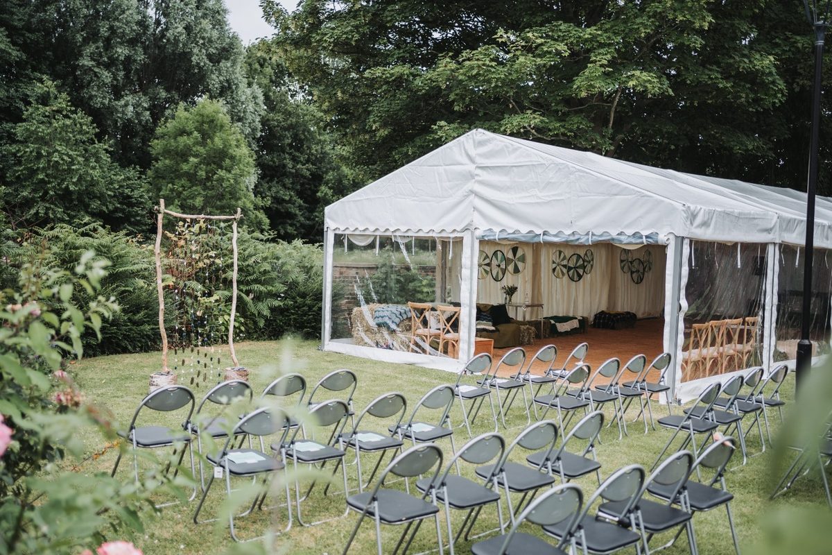 Frame marquee and rows of chairs set out for an outdoor wedding ceremony in a garden