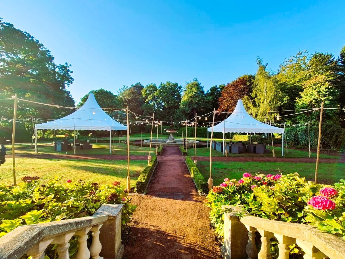 Pagoda marquees in a formal garden with festoon lighting strung along the walkway