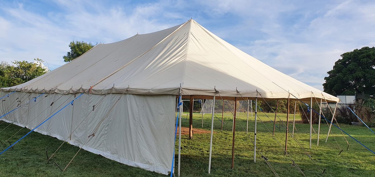 Cream canvas traditional pole marquee on a lawn, with wooden poles and one side open